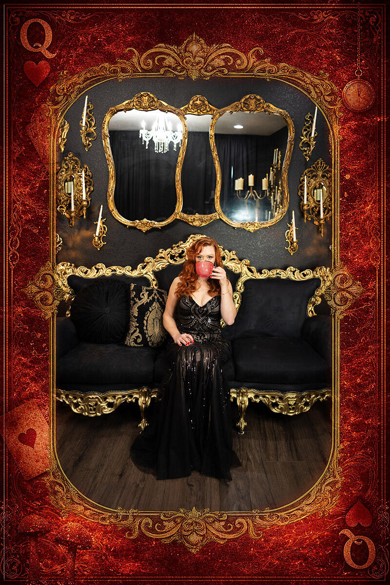 Queen of Hearts Conceptual Portrait Woman in a black gown holding a red teacup on an ornate black-and-gold sofa in a Queen of Hearts conceptual portrait.